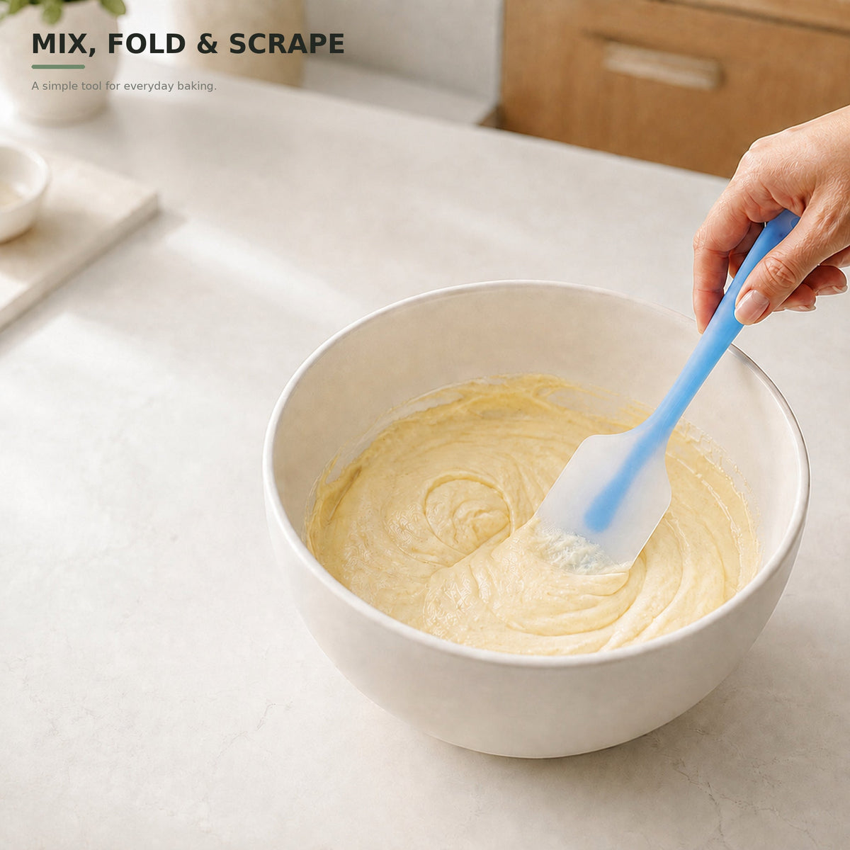 Blue silicone spatula mixing and folding batter in a bowl